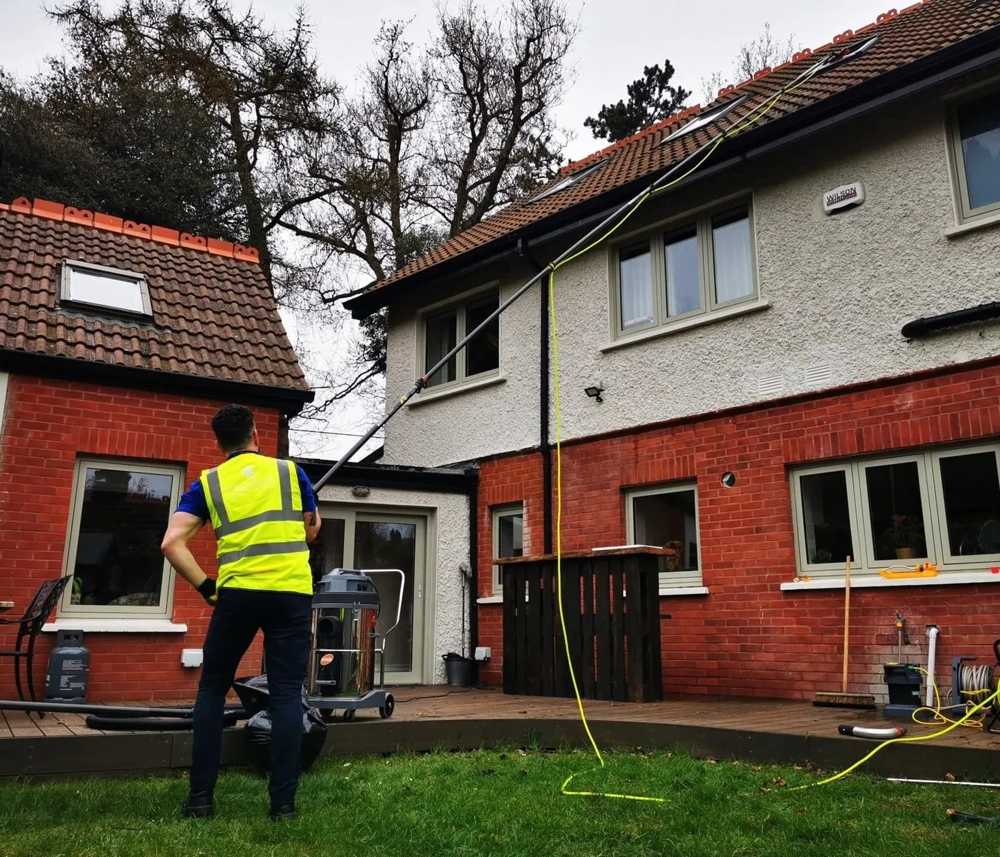 Premier cleaner clearing gutters on a red brick house