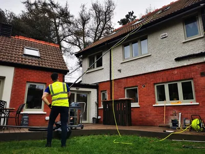 Premier cleaner clearing gutters on a red brick house