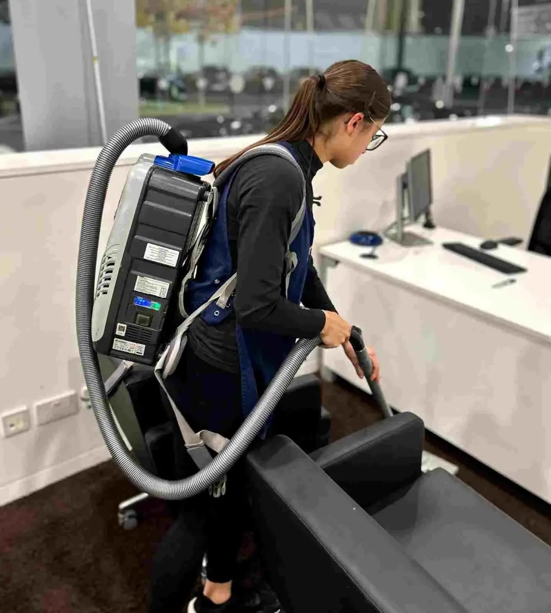 Premier cleaner using a backpack vacuum in a modern office