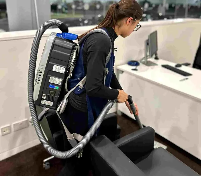 Premier cleaner using a backpack vacuum in a modern office